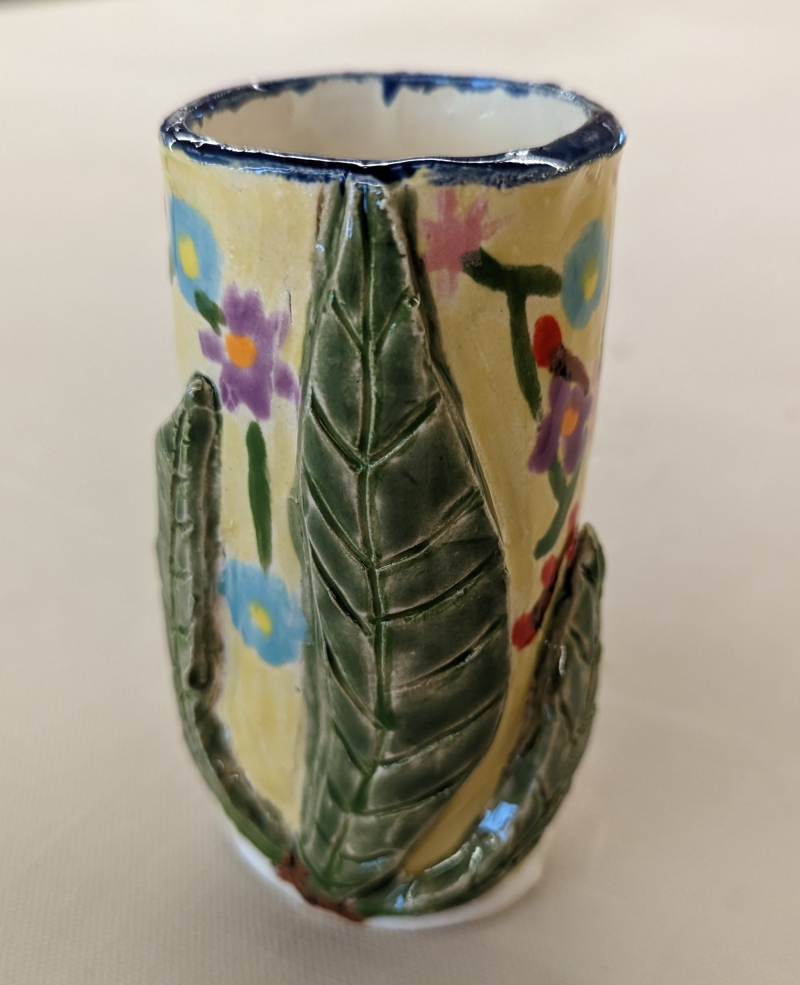 A ceramic cup decorated with leaves and flowers. It has a blue rim.