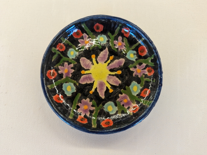 A ceramic plate, 3 inches small, with purple, red, and blue flowers on a black background.