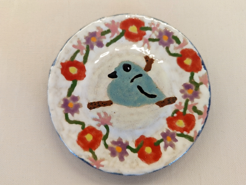 A ceramic plate with a blue bird and purple, pink, and red flowers painted on a white background.